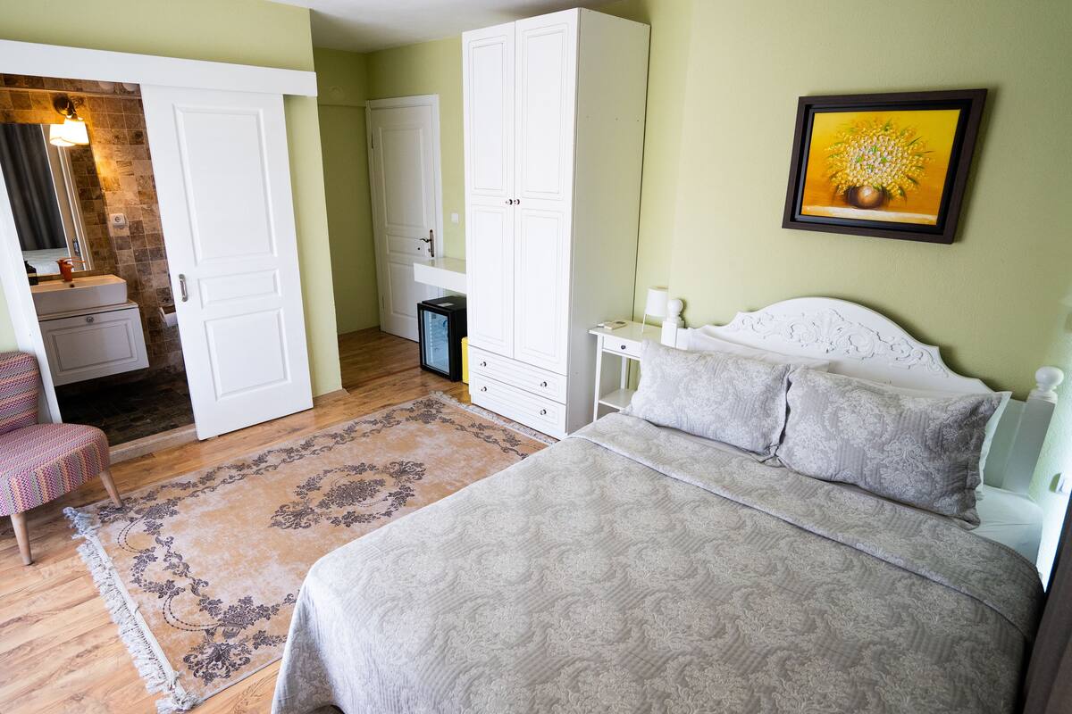 A bedroom with a bed, a chair, a wardrobe, a nightstand, and a framed picture on the wall.