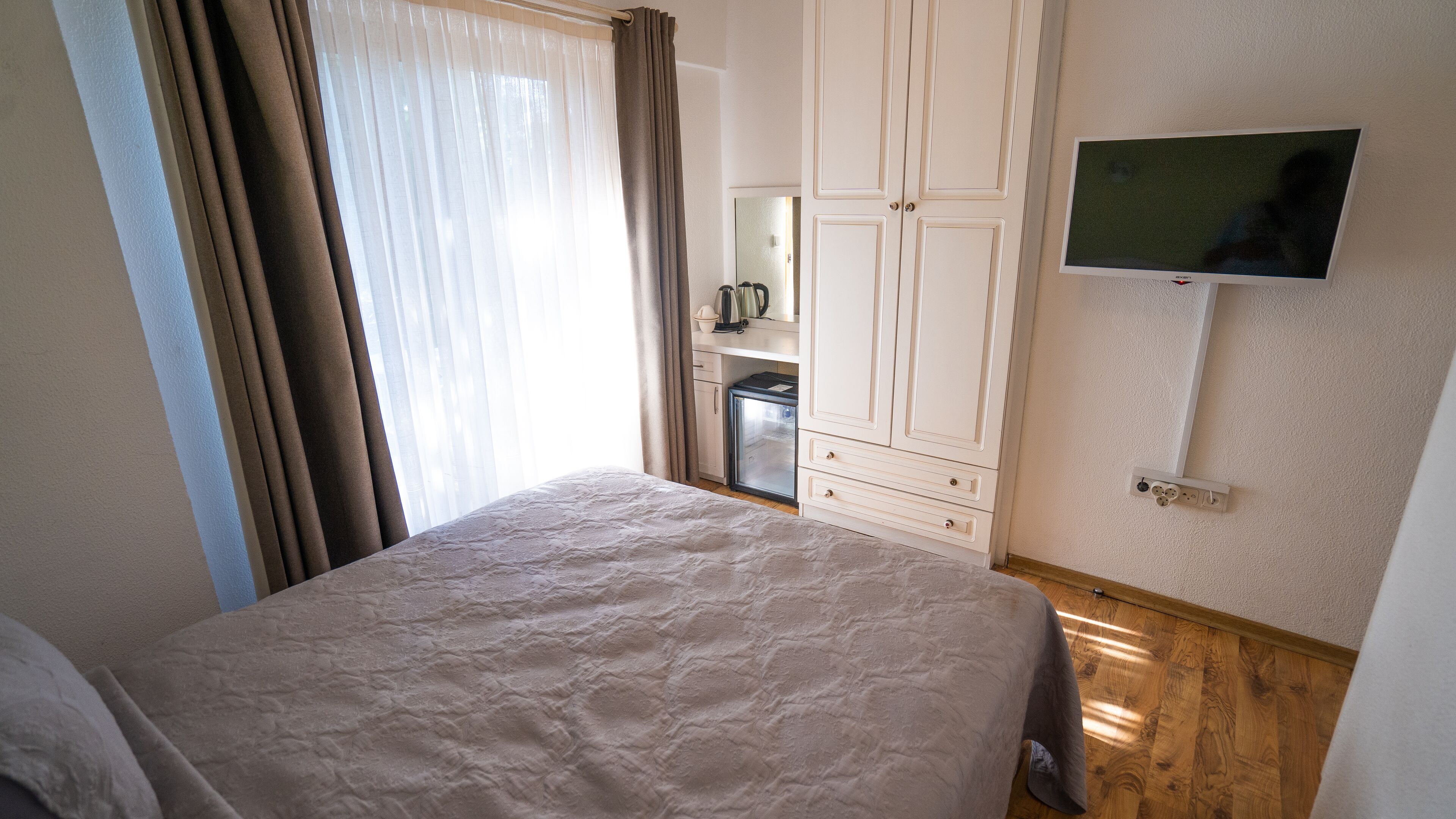 A bedroom with a bed, a wardrobe, a television, and a small kitchenette.