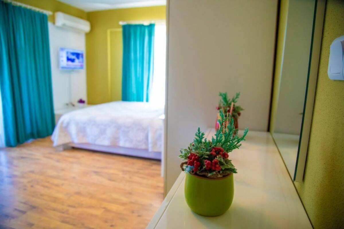 A hotel room with a bed, a green plant on a bedside table, and a television on the wall.