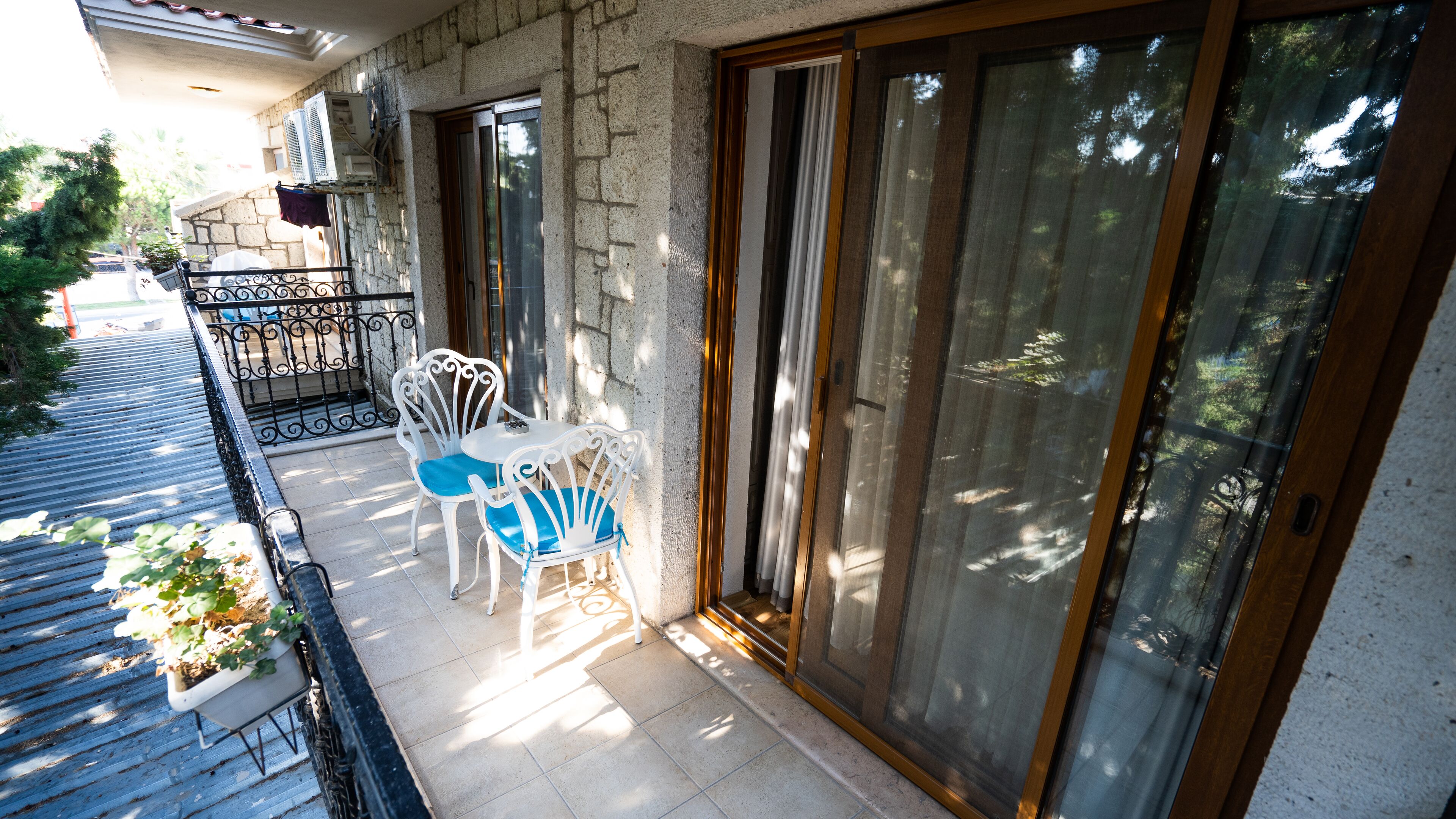 A balcony with a white chair and a small table, a stone wall, and a sliding glass door.