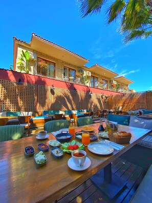 An outdoor dining area with a long table set for breakfast, surrounded by cushioned seating. - Alacati Private  (Cesme)