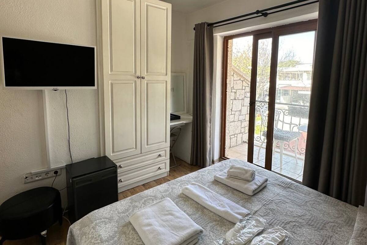 A hotel room with a bed, a TV, a wardrobe, a desk, and a view of the outdoors.