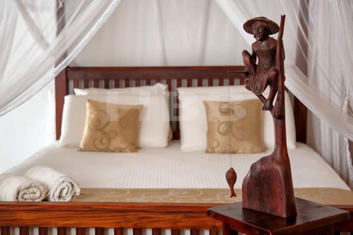 Un lit avec une tête de lit en bois, une literie blanche et une sculpture décorative en bois posée sur une table de chevet.