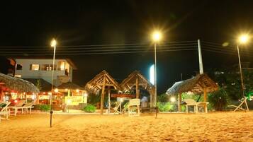 A beachside resort with thatched-roof huts, a pool area, and a building with multiple windows.