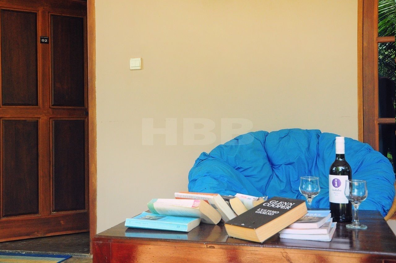 A room with a wooden door, a blue chair, a table with books and wine glasses.