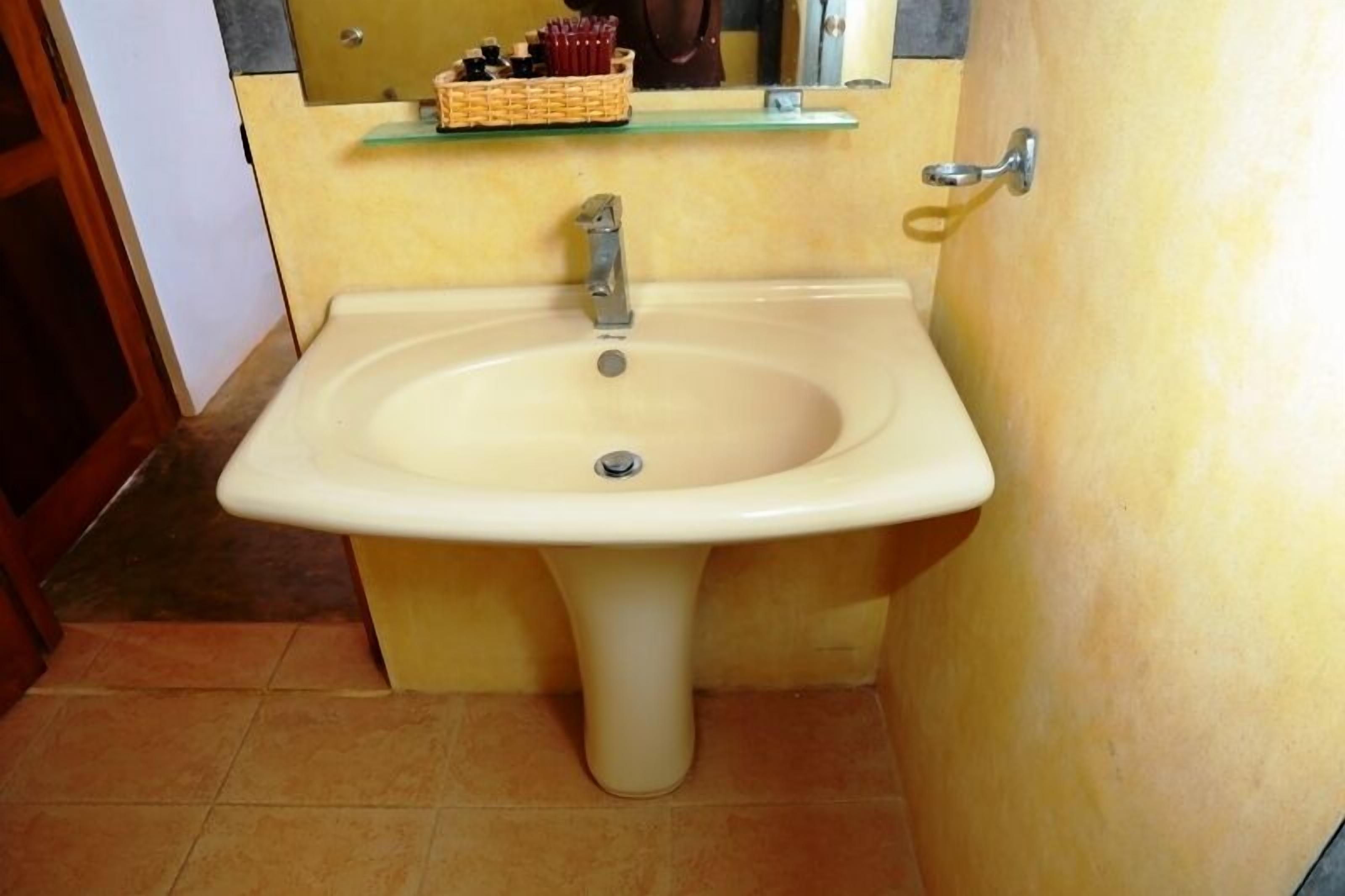 Un bagno con un lavandino color beige, uno specchio e uno scaffale con articoli da toilette.