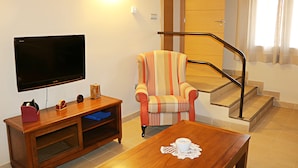 Un salon doté d’un téléviseur à écran plat, d’un fauteuil à rayures, d’une table basse en bois et d’un escalier muni d’une main courante.