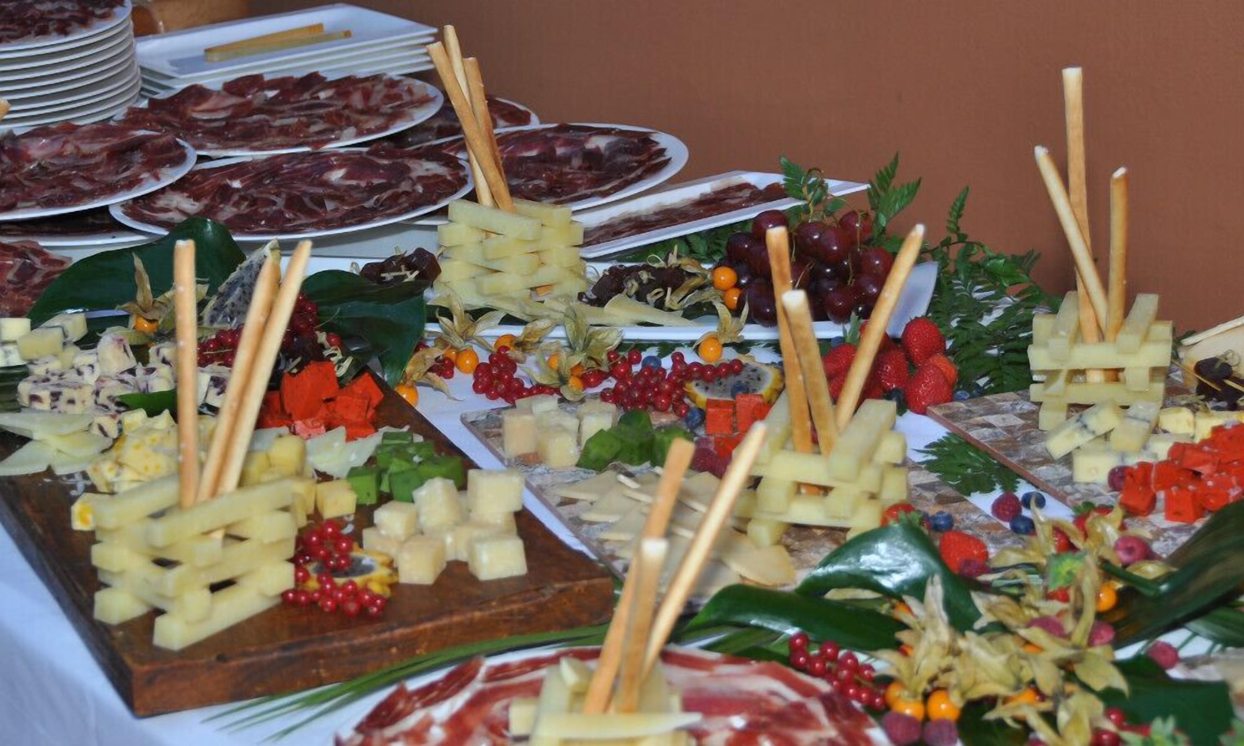 Een buffet met diverse gerechten, waaronder vleeswaren, kazen, fruit en groenten.