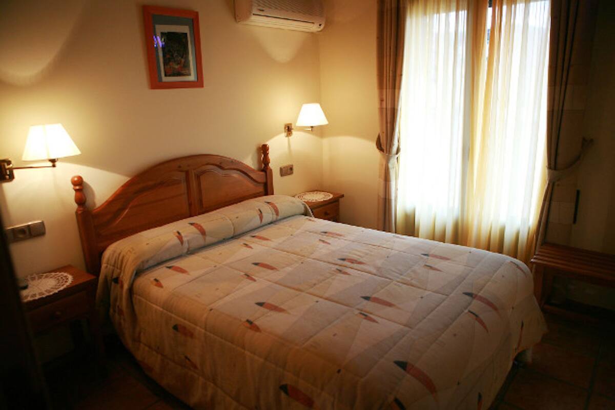Een netjes opgemaakt bed met een sprei, twee bedlampjes en een ingelijste foto aan de muur.