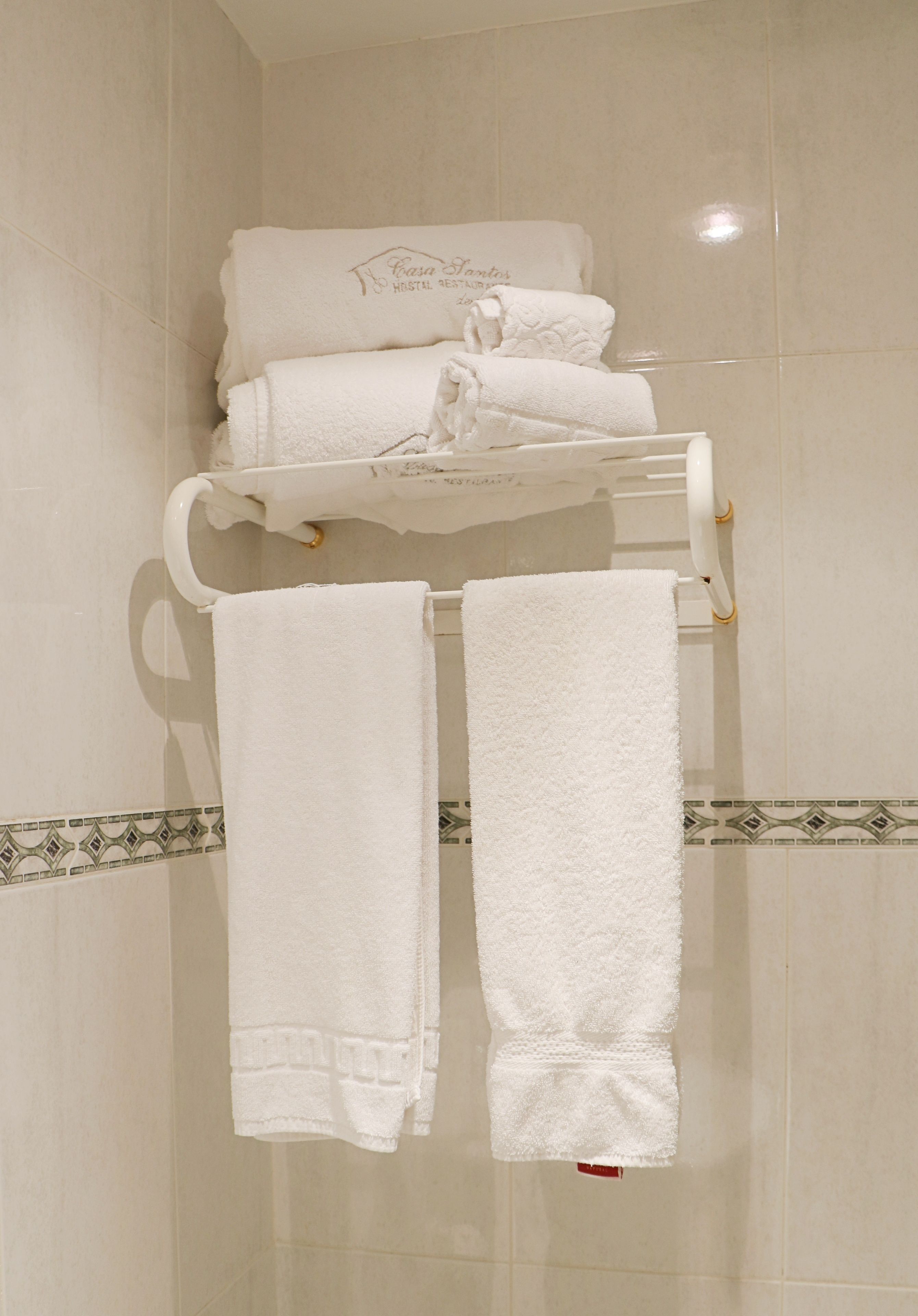 A bathroom with a white tiled wall, a towel rack with folded towels, and a decorative border on the floor.