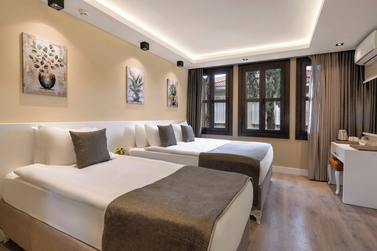 A hotel room with two beds, a desk, and a window with curtains.