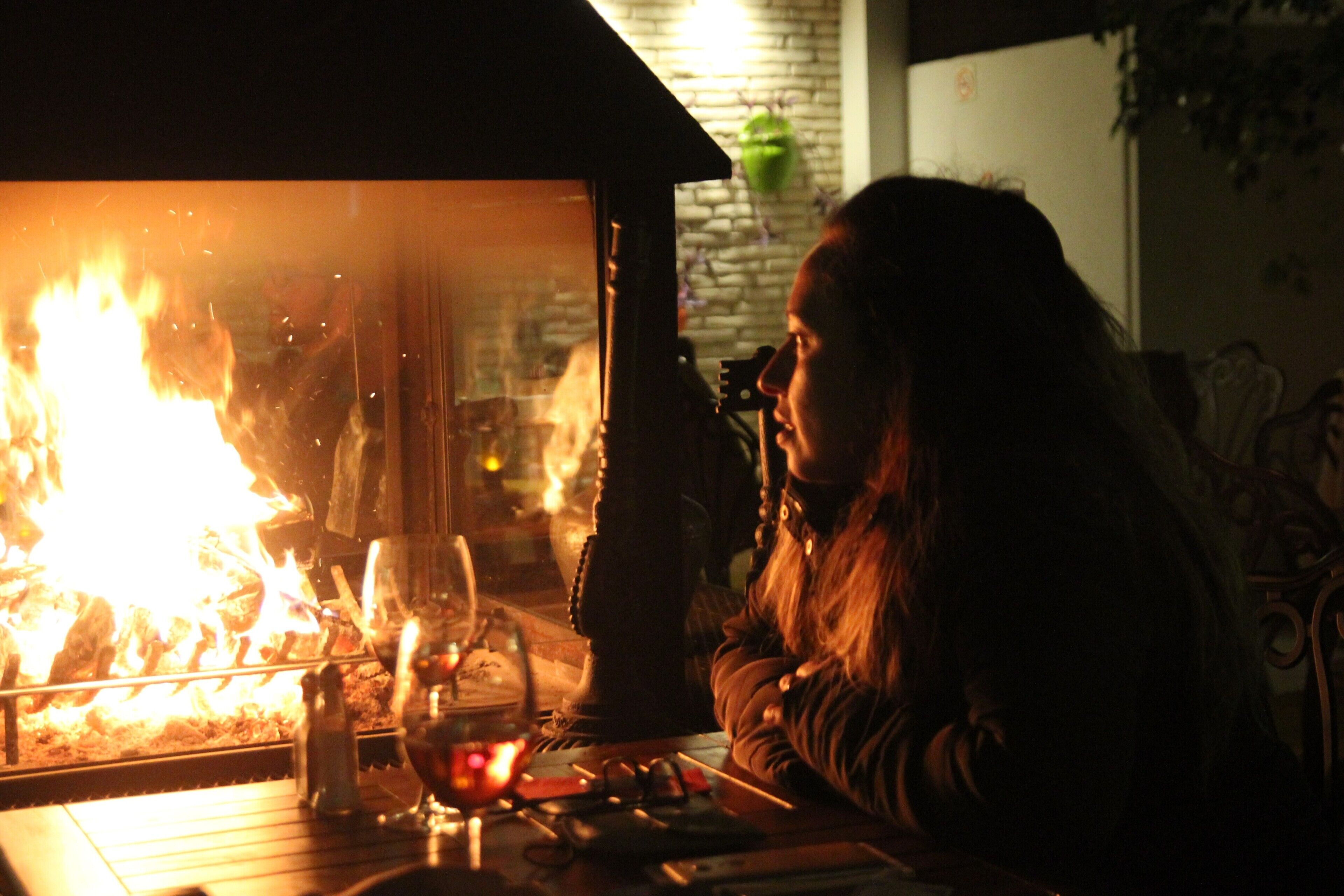 A person sitting at a table with a fire visible through a glass partition, a salt shaker, and a glass on the table.