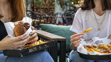 Duas pessoas sentadas à mesa com uma bandeja de comidas, incluindo um hambúrguer e batatas fritas.