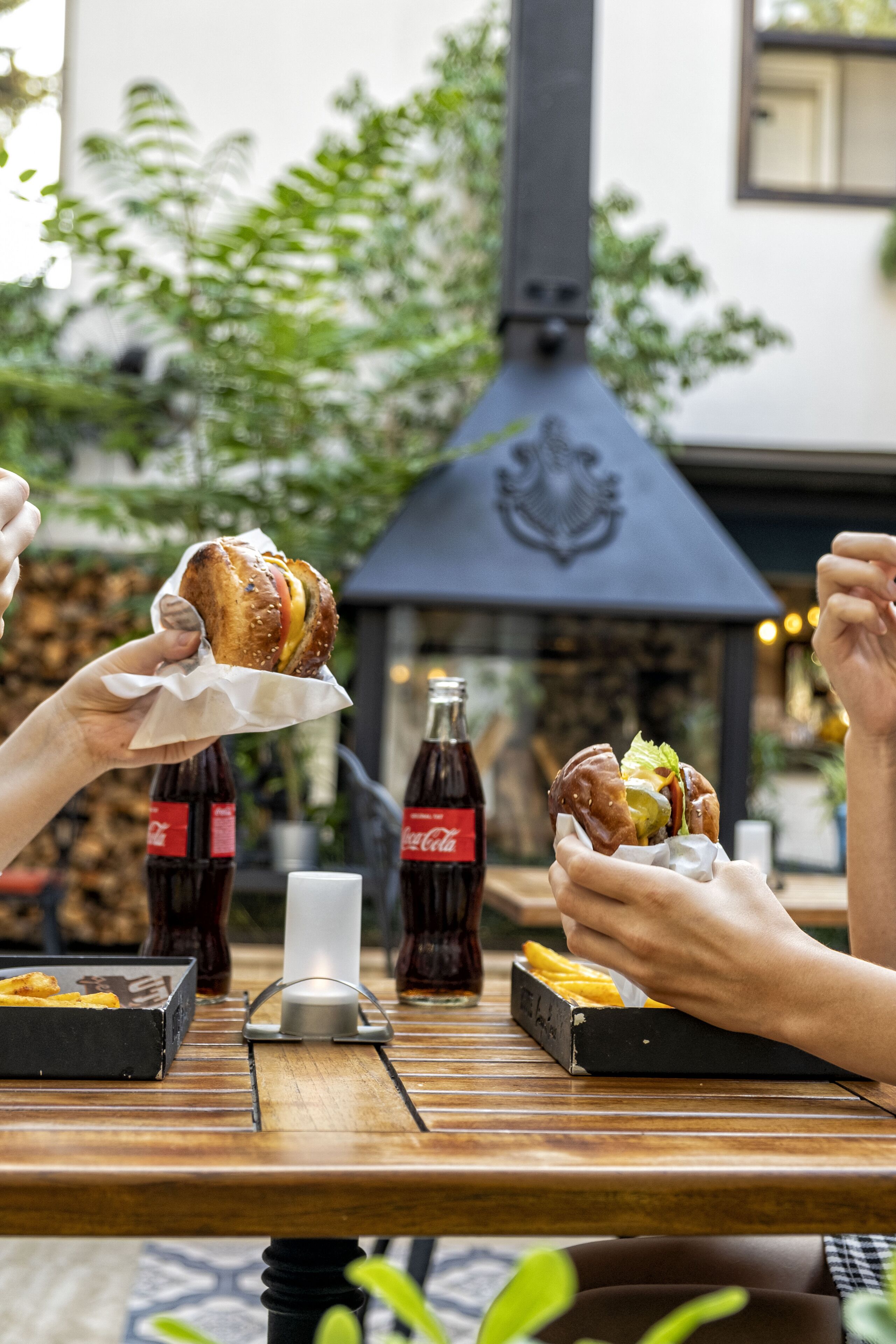 Una mesa de madera con comida, dos botellas de Coca-Cola y una vela.
