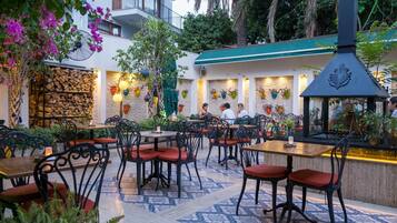 An outdoor dining area with wooden tables and chairs, surrounded by potted plants and flowers.