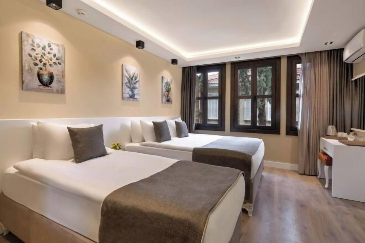 A hotel room with two beds, a desk, and a window with curtains.