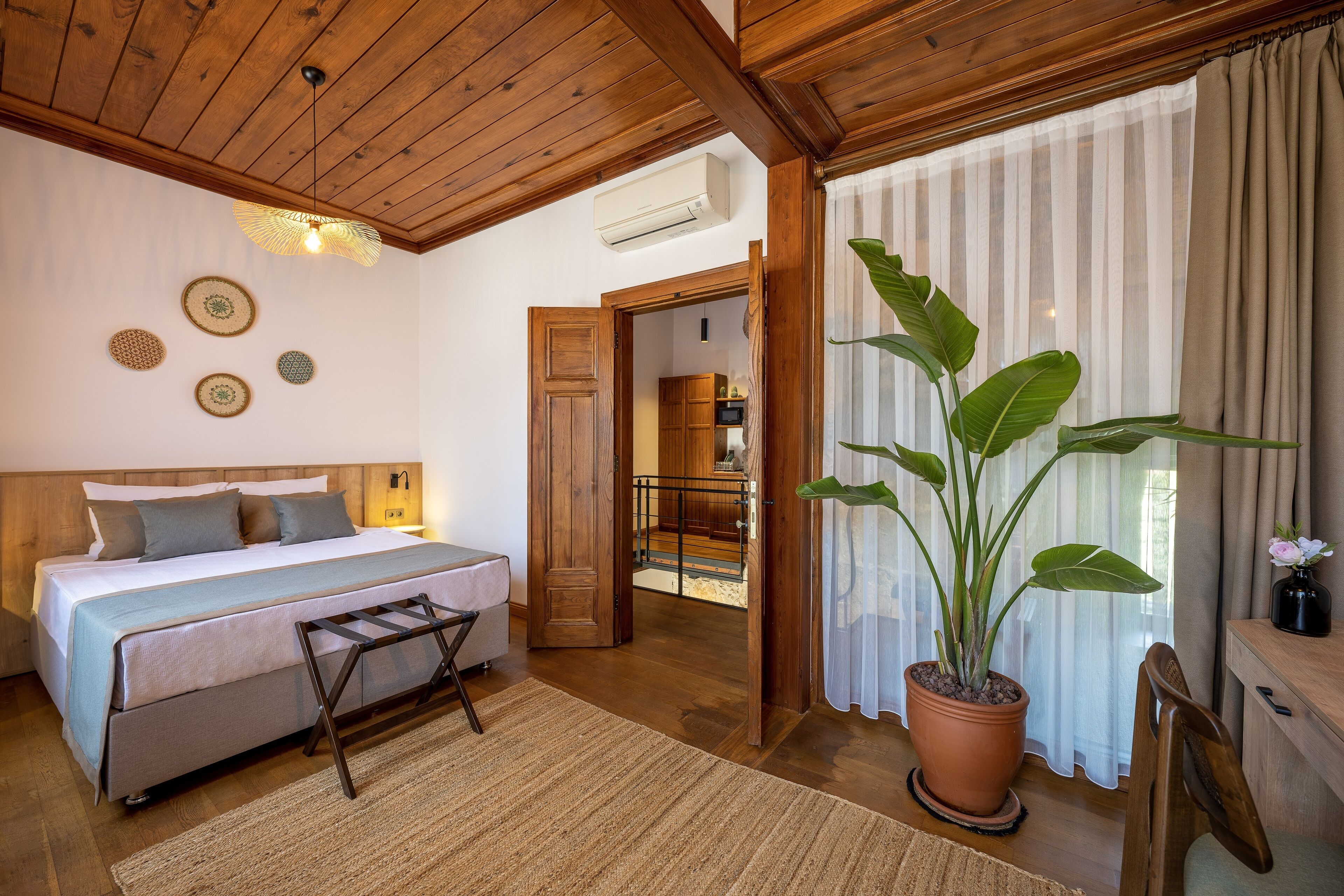 A bedroom with a bed, a wooden ceiling, a potted plant, and a view of a balcony.