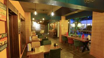Un restaurante con mesas y sillas de madera, luces colgantes y una zona de bar.