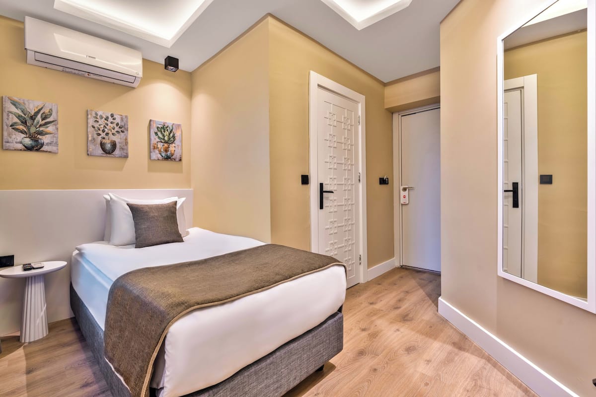 A hotel room with a bed, bedside table, air conditioning unit, and artwork on the walls.