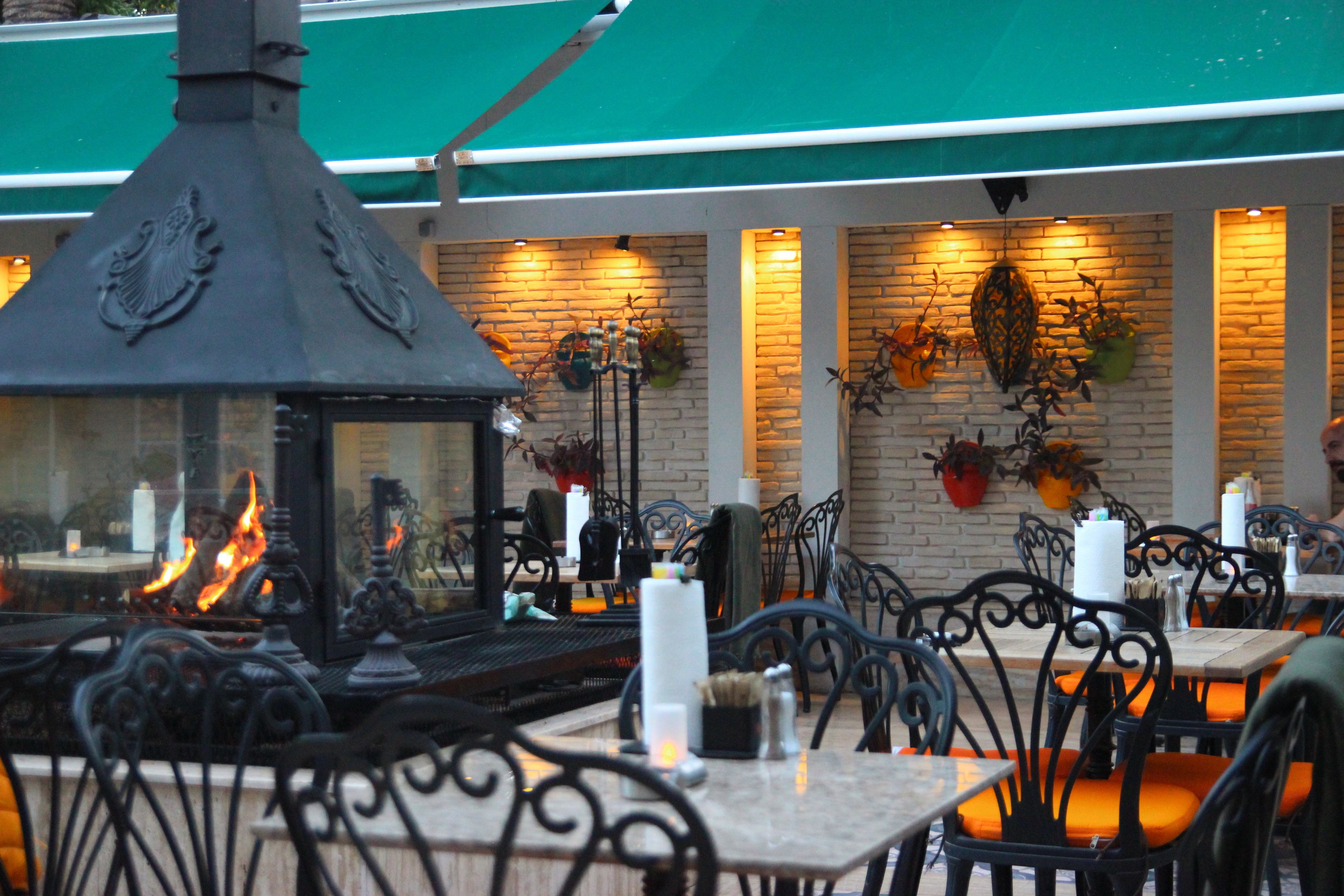 An outdoor dining area with brick walls, metal chairs, and a central fire feature.