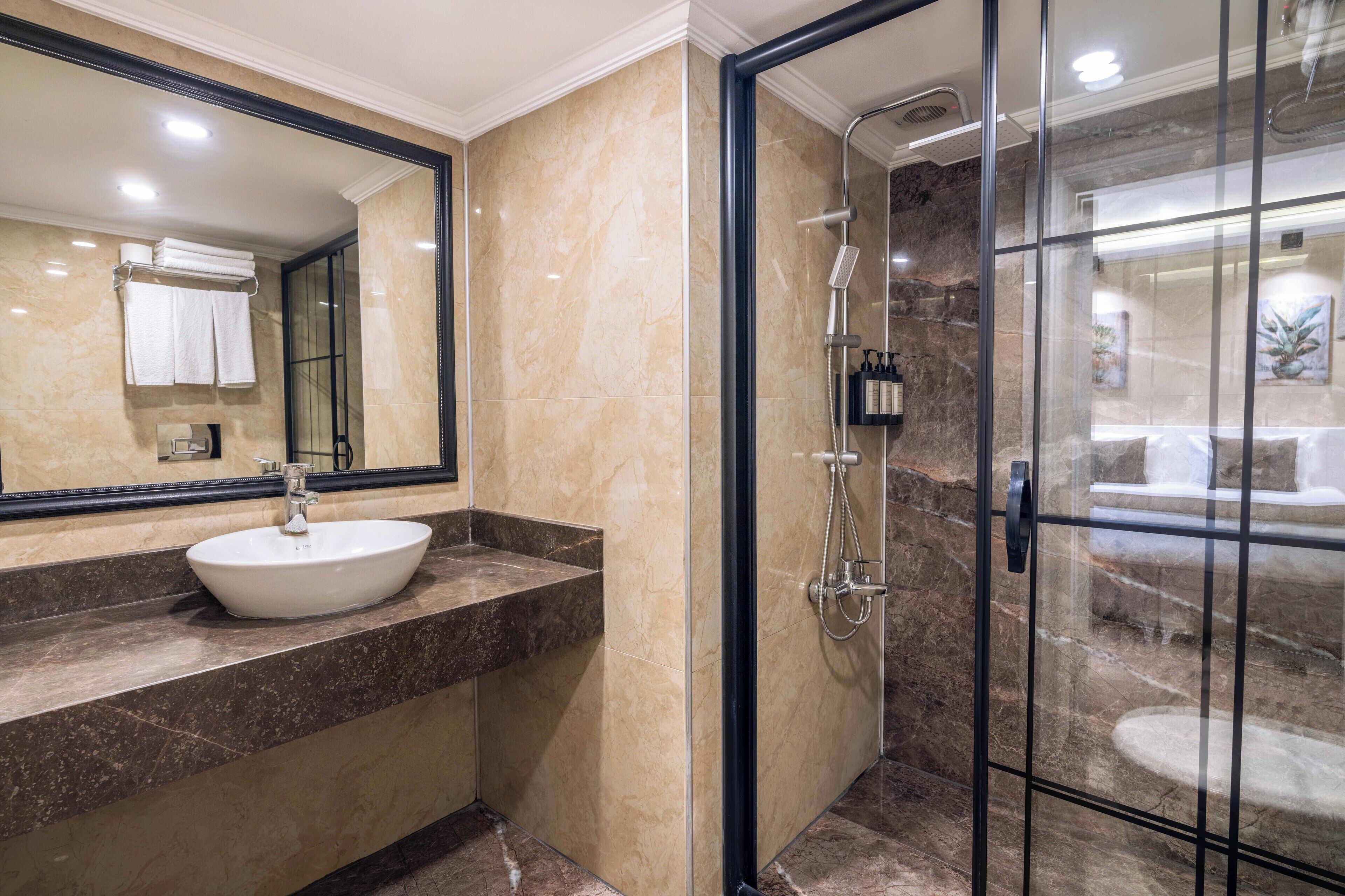 A modern bathroom with a marble vanity, a large mirror, and a glass-enclosed shower area.