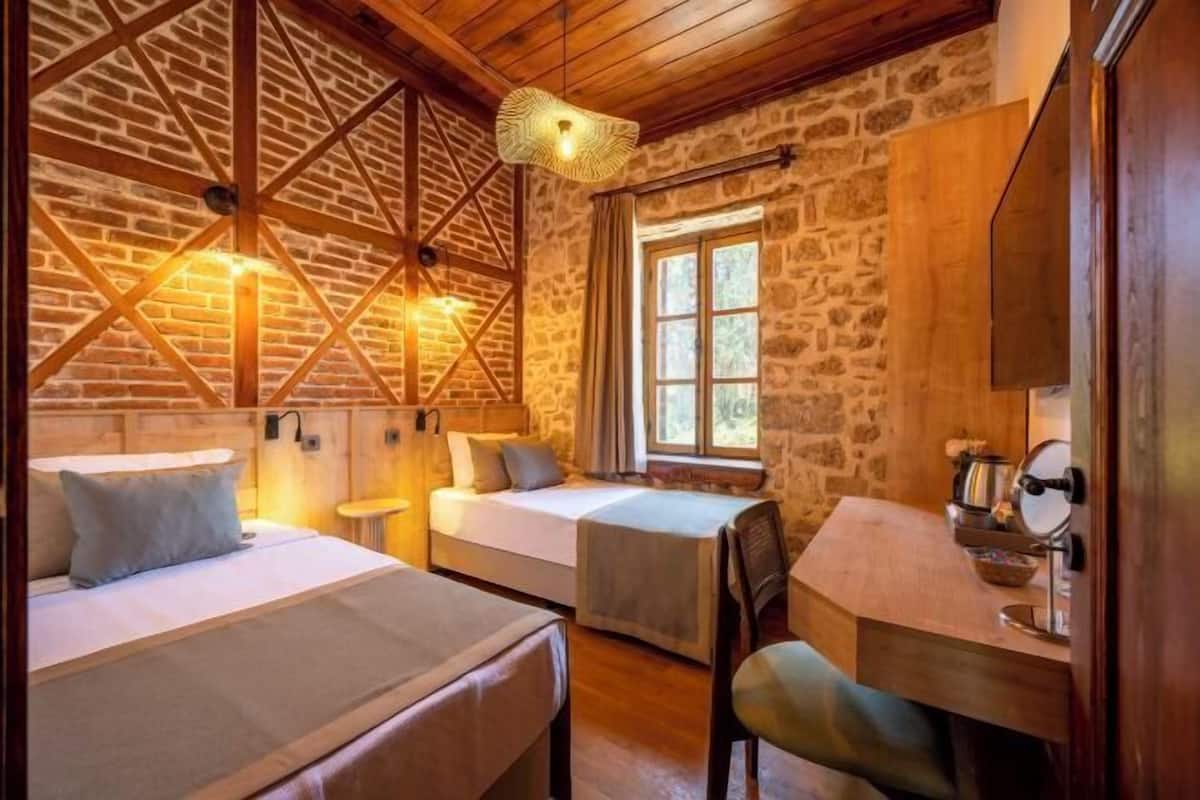 A rustic room with two beds, a small table, a chair, and a stone wall.