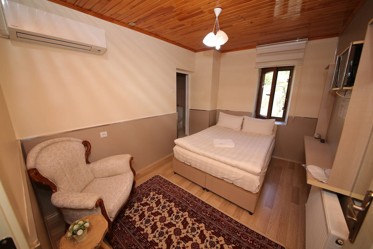 Un dormitorio con cama, una silla, una mesita con un jarrón y una ventana.