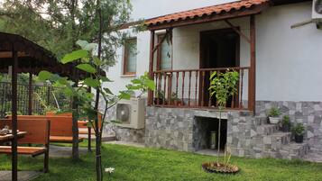 A residential building with a stone facade, a balcony with wooden railings, and a small garden area with benches and potted plants.