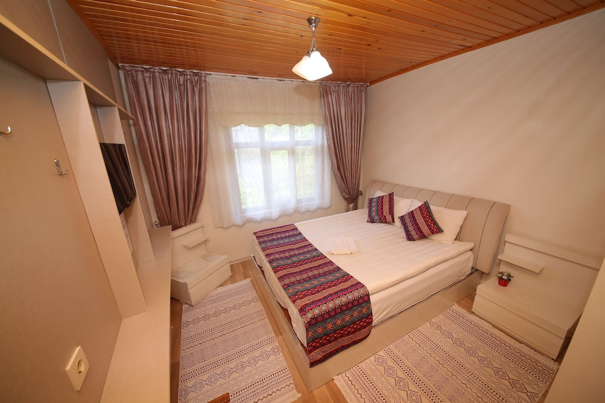 Un dormitorio con cama, cortinas, ventilador de techo y una mesita de noche.