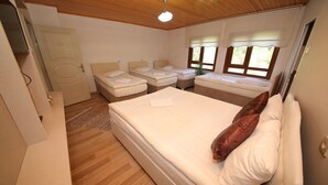 A room with a large bed, two smaller beds, wooden flooring, a ceiling fan, and windows with curtains. - Emiroglu Konak (Safranbolu)