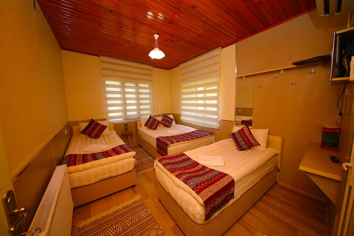 Habitación de hotel con tres camas, techo de madera y un pequeño escritorio con espejo.