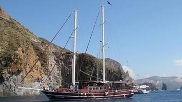 A large sailing boat docked near rocky cliffs.