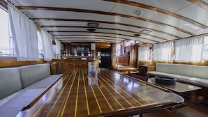 A dining area with a long wooden table, cushioned seating, and a bar counter. - Tersane IV (Palermo)