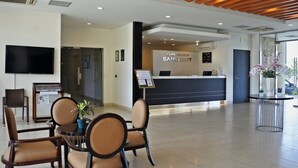 Un vestíbulo de hotel con una recepción, sillas, un televisor y una planta.