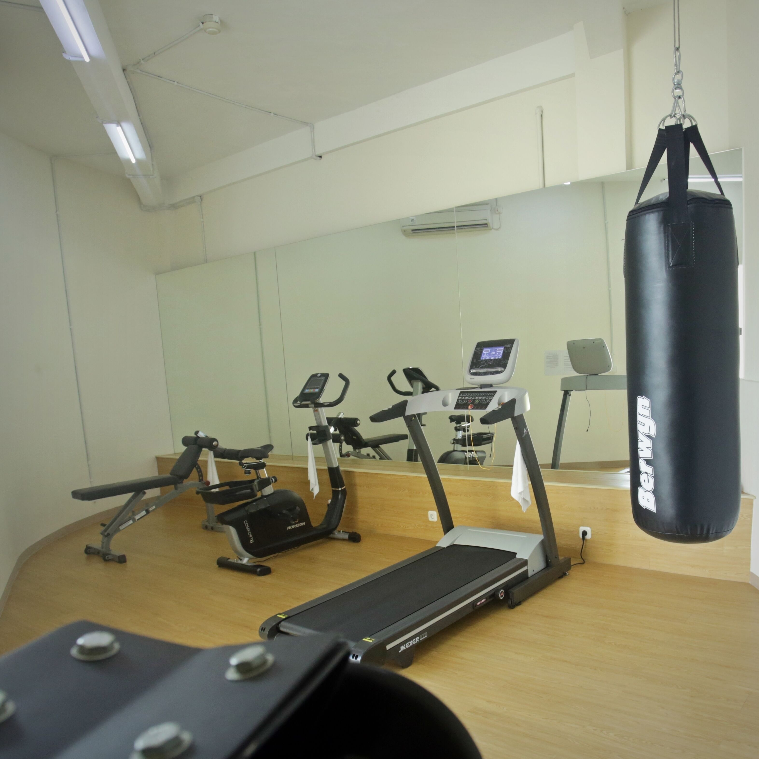 A gym with exercise equipment including treadmills and an elliptical, a punching bag, and a mirrored wall.