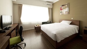 Habitación de hotel con cama, escritorio con computadora, silla, mesita con planta y ventana con cortinas.