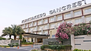Un hotel llamado 'Kurta Keso Sanctuary' con fachada moderna, entrada cubierta y jardines ajardinados.