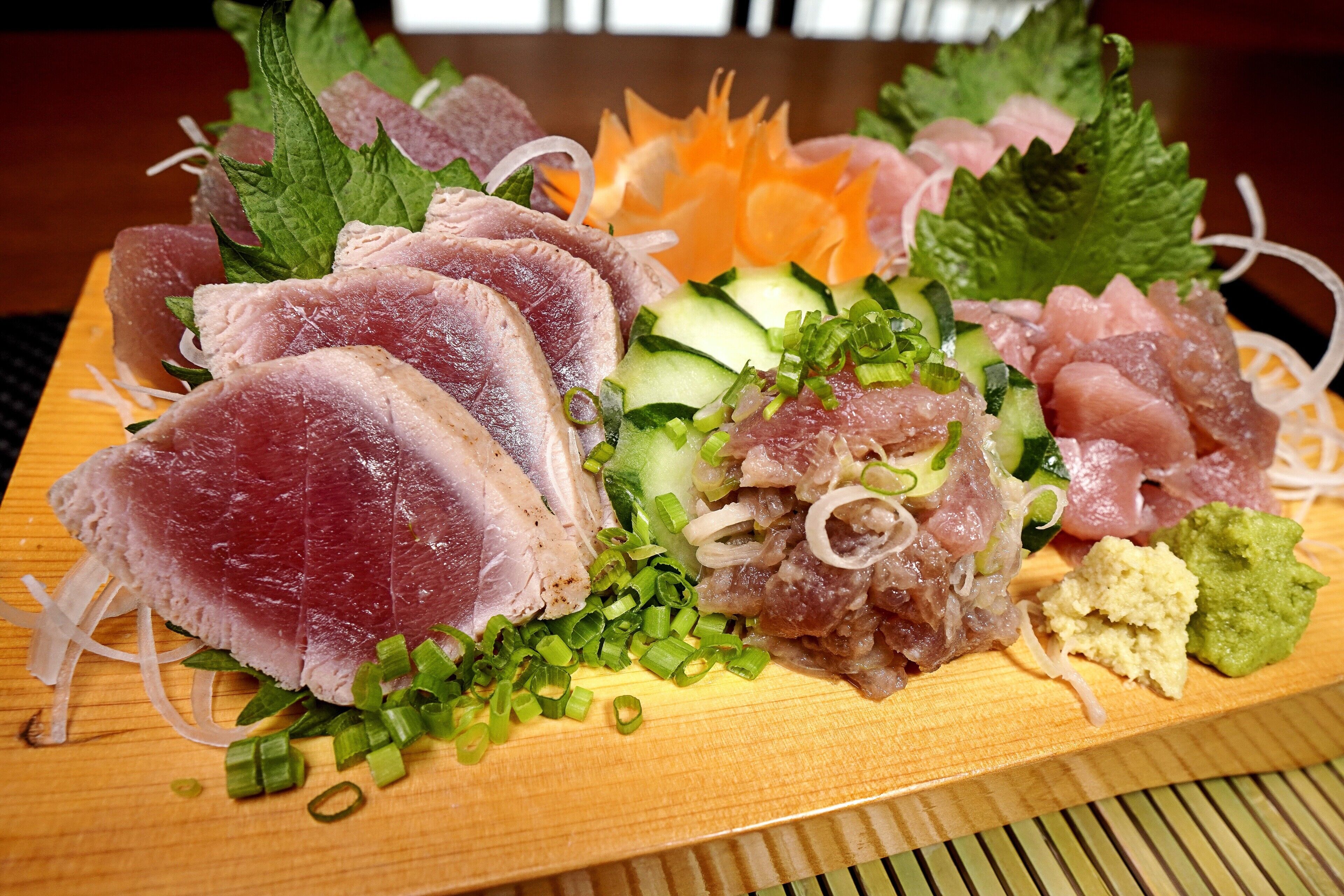 A wooden board with various types of raw fish and garnishes.