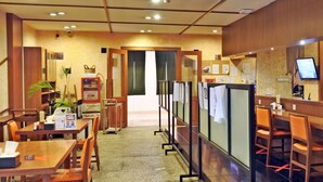 Un restaurante con mesas y sillas de madera, una barra con menú y vistas de la calle a través de un panel de vidrio.
