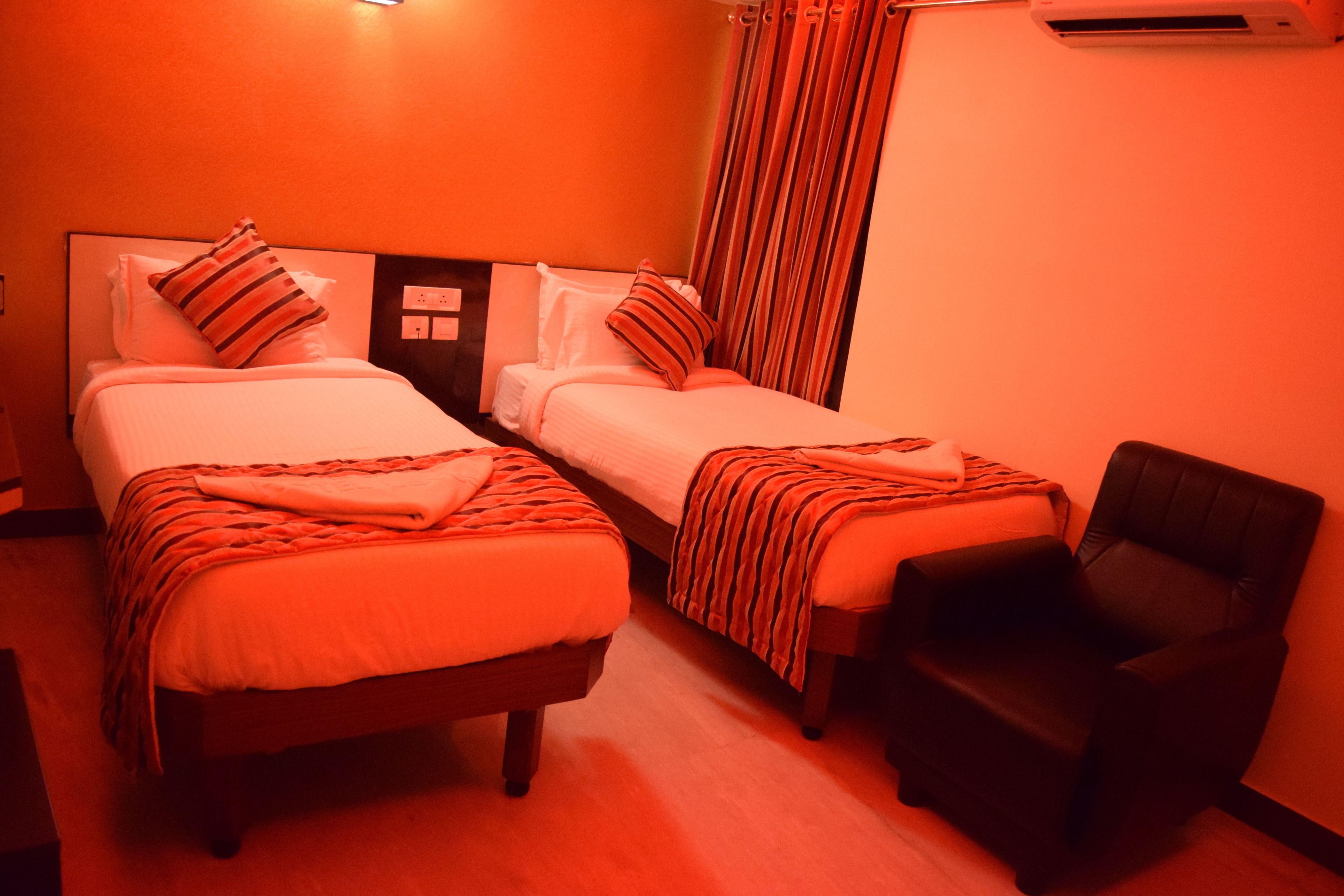 A hotel room with two beds, a chair, and an air conditioning unit.