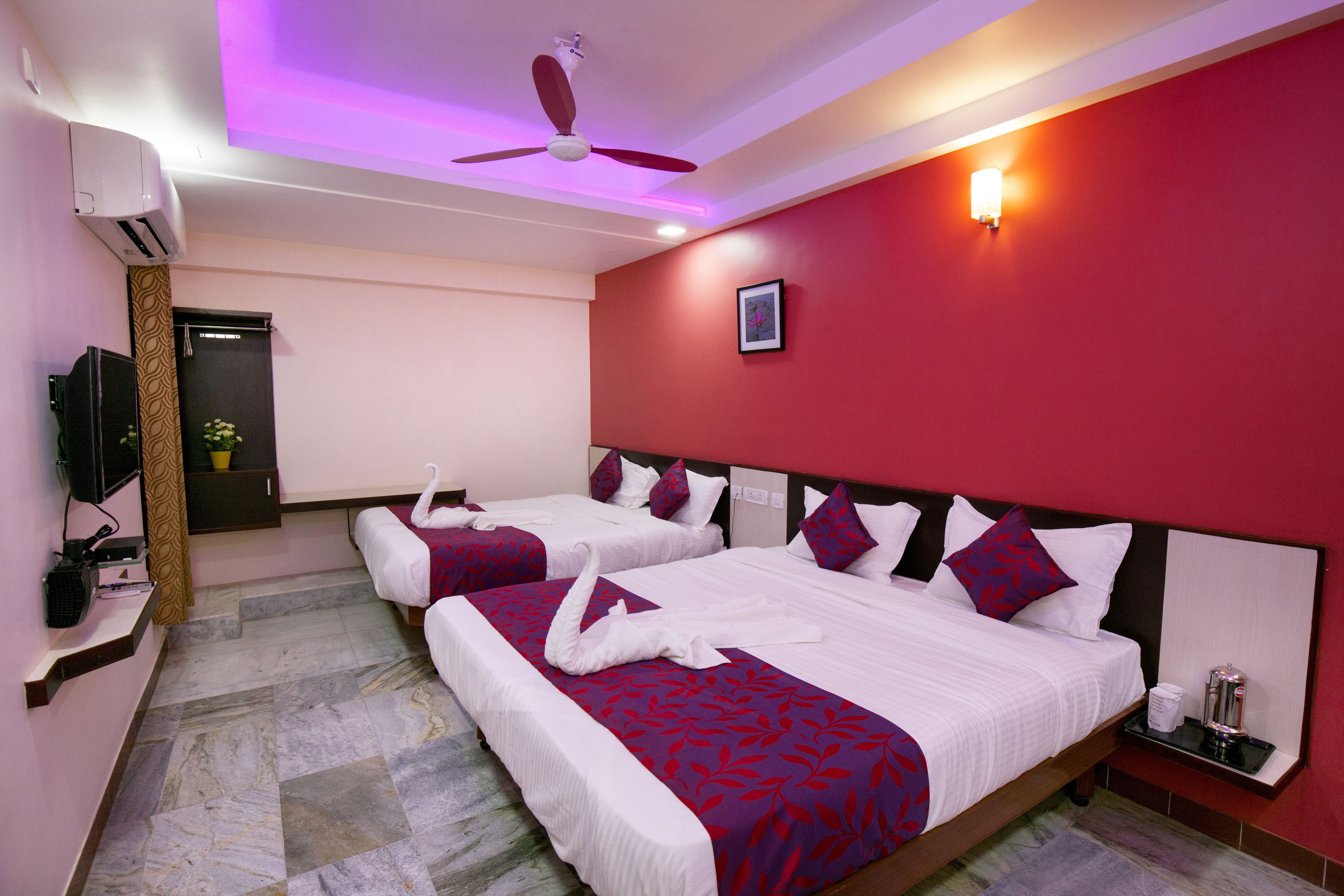 A hotel room with two beds, red walls, a ceiling fan, and a mounted TV.