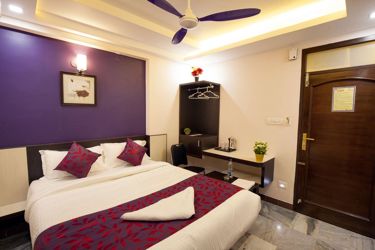 A hotel room with a bed, a desk, a mirror, a door, and a ceiling fan.