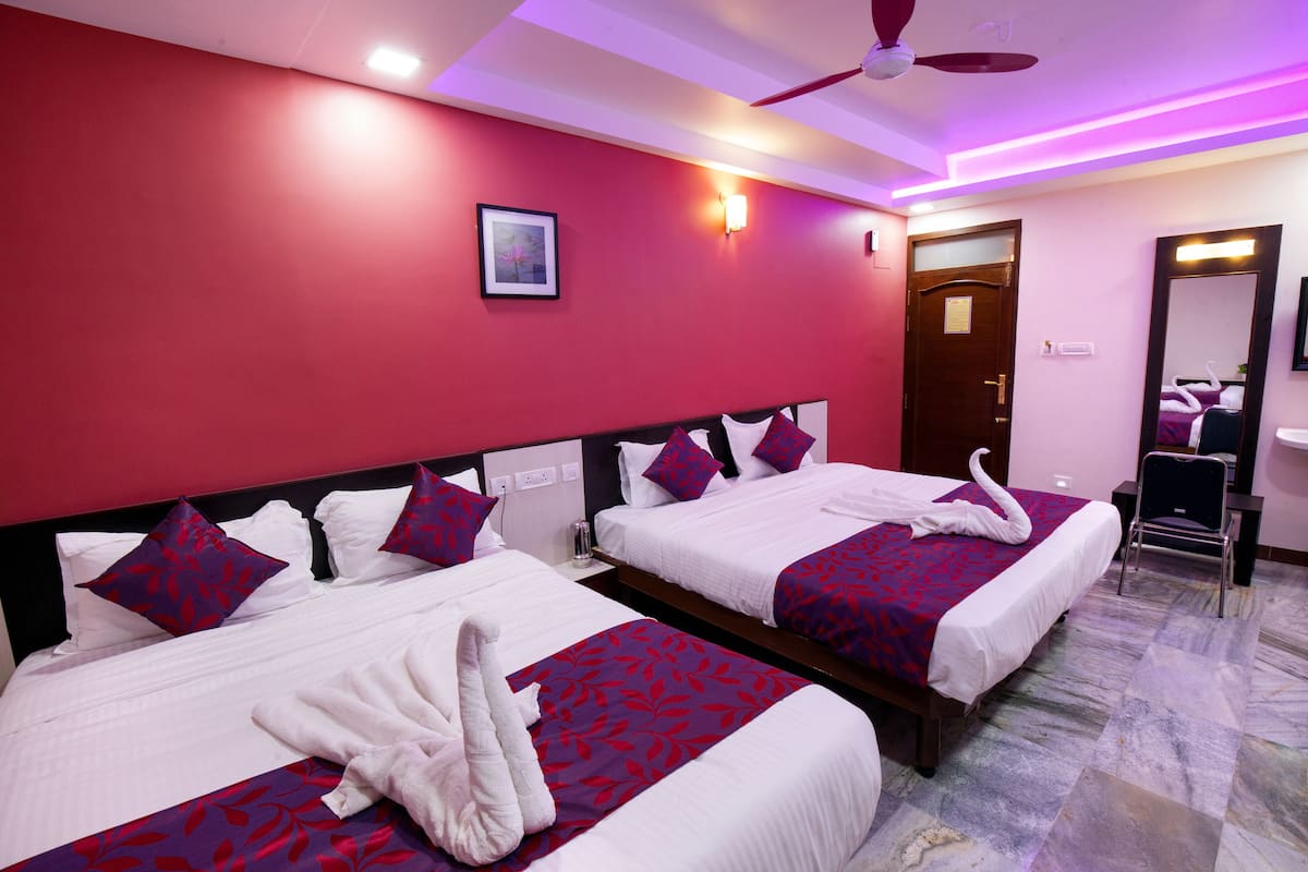 A hotel room with two beds, each with a red and white bedspread, white pillows, and a white bathrobe. There is a ceiling fan, a framed picture on the wall, and a mirror above the door.