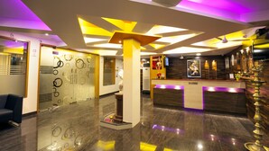 A modern lobby with a reception desk, a decorative column, and a glass wall with circular patterns. - Hotel Lotus (Madurai)