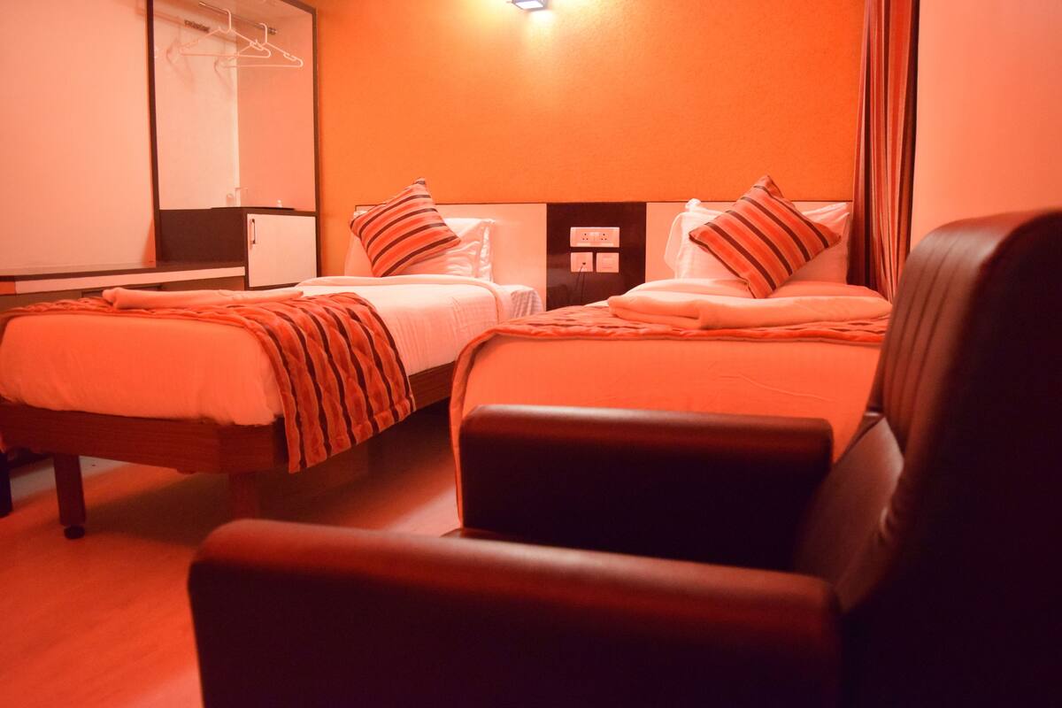 A hotel room with two beds, a chair, a wardrobe, and a mirror.