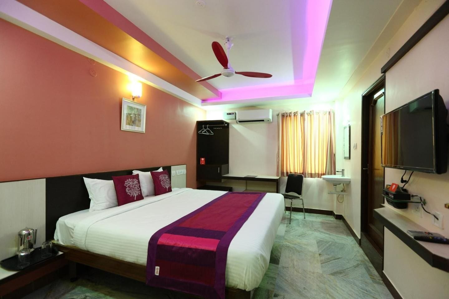 Quarto de hotel com cama, secretária, cadeira, televisão e ar condicionado.