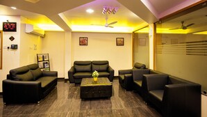 A modern living room with black leather sofas, a central ottoman, and a ceiling fan. - Hotel Lotus (Madurai)