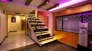 A modern hotel lobby with a marble floor, a staircase with illuminated steps, and a water dispenser. - Hotel Lotus (Madurai)