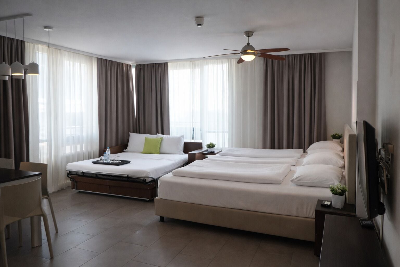 Habitación de hotel con dos camas, un escritorio, una silla, un televisor y un ventilador de techo.