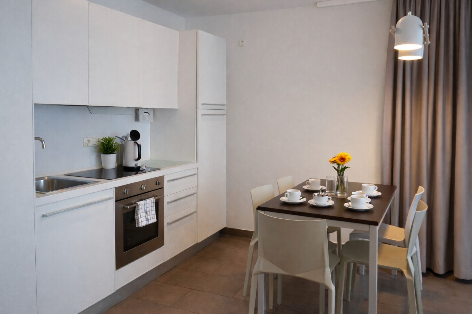 Una cocina moderna con armarios blancos, horno integrado y comedor con mesa lista para dos.